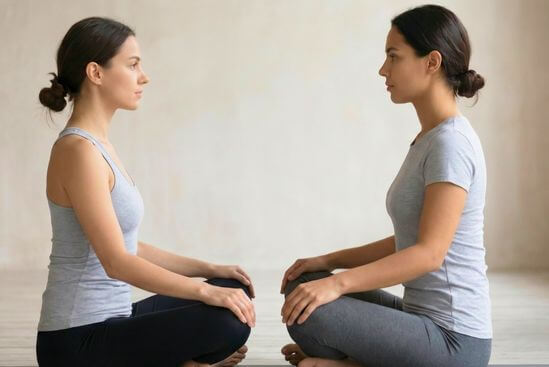 Duas pessoas sentadas frente a frente totalmente vestidas em exercício de conexão visual, esclarecendo dúvidas sobre se é preciso tirar a roupa no workshop de Tantra.