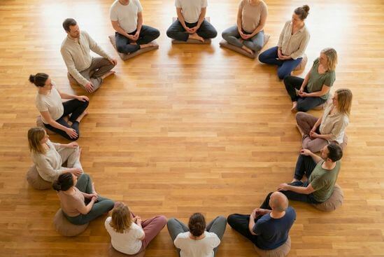 Grupo de pessoas vestidas confortavelmente sentadas em círculo no chão, demonstrando as dinâmicas de grupo no Tantra e o acolhimento inicial.