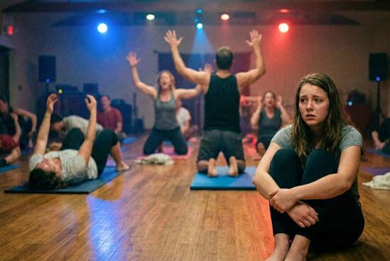Grupo em retiro intenso com música e respiração fortes, mulher assustada em destaque durante ativação da kundalini.