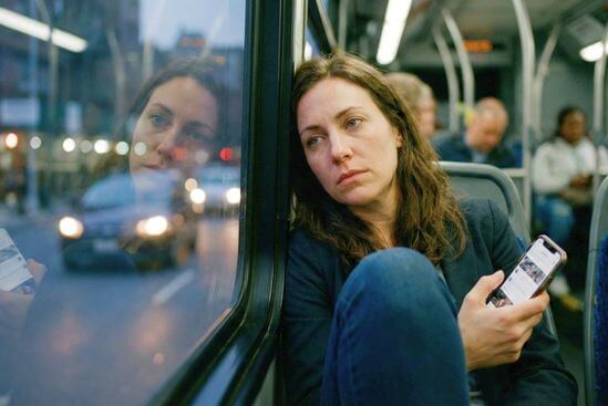 Mulher exausta no ônibus, olhar distante e celular na mão, mostrando sinais de esgotamento mental no trabalho.