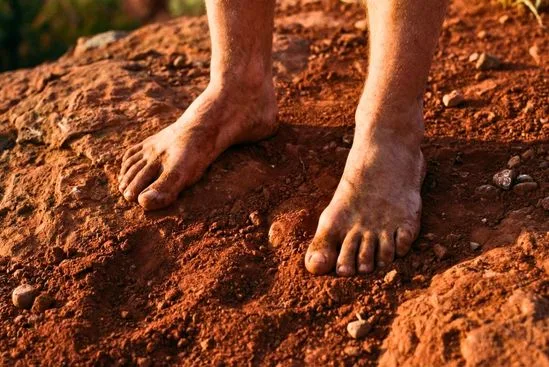 Pés descalços em contato firme com terra vermelha, ilustrando o que são chakras no corpo e a conexão com a base.