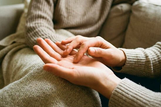 Uma mão repousa aberta no colo enquanto a outra explora suavemente a palma, praticando toque consciente no casal.