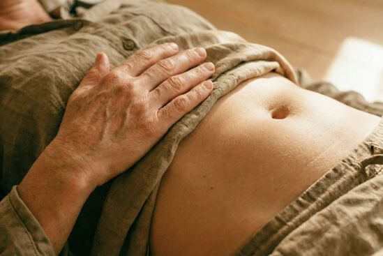Detalhe aproximado de mão repousada sobre o abdômen sentindo a respiração, ilustrando a prática de presença e o Tantra contemporâneo.