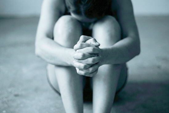 Detalhe das mãos de uma pessoa abraçando os próprios joelhos com força, simbolizando o bloqueio emocional e a necessidade de proteção do corpo.