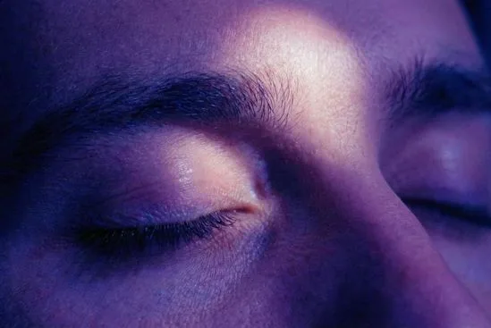 Close-up de olho fechado em ambiente de penumbra índigo, ilustrando a visão interior e os 7 chakras e seus significados.