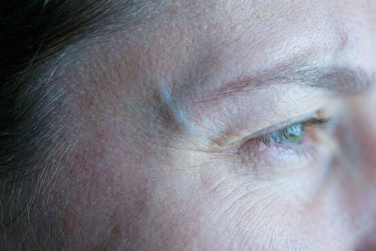 Detalhe macro da pele tensa ao redor dos olhos de uma pessoa sob luz artificial, simbolizando como chegar em casa menos cansado(a) do trabalho e o excesso de estímulos.