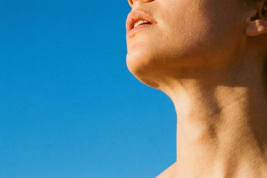 Perfil do pescoço alongado contra um céu azul claro, simbolizando a comunicação e chakras e sistema nervoso na expressão.