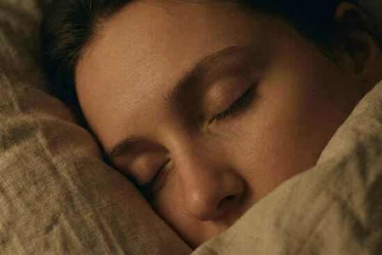 Detalhe de rosto sereno com olhos fechados na penumbra, exemplificando como praticar presença no dia a dia e relaxamento do rosto antes de dormir.