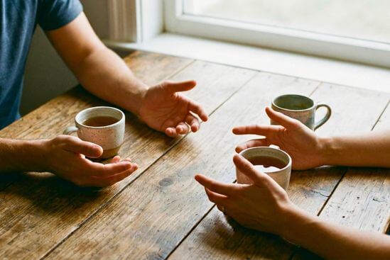 Mãos em gesto de diálogo sobre mesa com chá, simbolizando uma conversa sobre o que acontece em uma sessão de massagem tântrica.