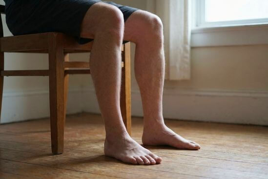 Pessoa sentada, pés descalços bem plantados no chão, joelhos flexionados, praticando um grounding suave.
