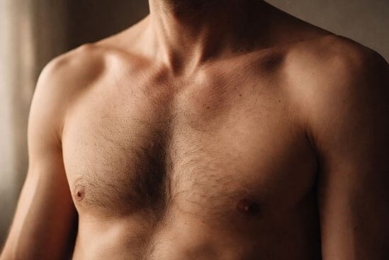 Fotografia íntima de torso ou mãos masculinas em repouso com luz natural suave e textura de pele visível, representando a masculinidade saudável que emerge quando a armadura emocional se afrouxa.