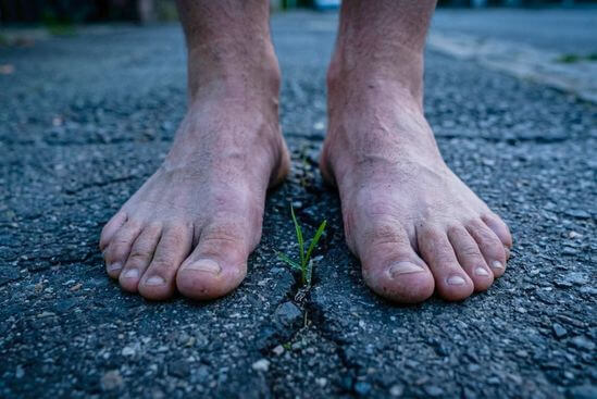 Pés descalços plantados em asfalto urbano com detalhe de rachadura, simbolizando Meditação Dinâmica Osho contraindicações.
