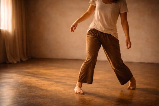 Fotografia de corpo em movimento inicial e hesitante, com roupa cotidiana em espaço interior anônimo e luz lateral quente, representando o momento em que a prática começa antes da confiança — o que fazer a meditação nataraj revela sobre o próprio autocontrole.