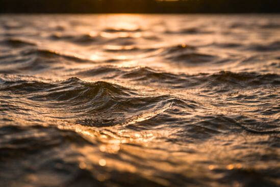 Fotografia de superfície de lago com ondulações irregulares e reflexos fragmentados de luz de fim de tarde, evocando a metáfora central do artigo — que nenhum lago agitado fica liso por obediência — e o que isso revela sobre quem tenta a meditação nataraj para iniciantes começando pela quietude.
