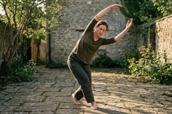 Pessoa em movimento físico amplo com pés plantados no solo e eixo corporal claro em espaço aberto com luz matinal lateral, representando o corpo em movimento consciente como porta honesta para a meditação para mente acelerada.