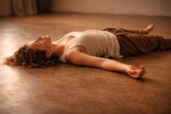 Fotografia de corpo deitado em repouso real após movimento, com luz natural lateral e espaço interior simples, traduzindo os benefícios da meditação Nataraj — o silêncio orgânico que nasce depois que o corpo encontrou passagem, diferente de qualquer quietude imposta.